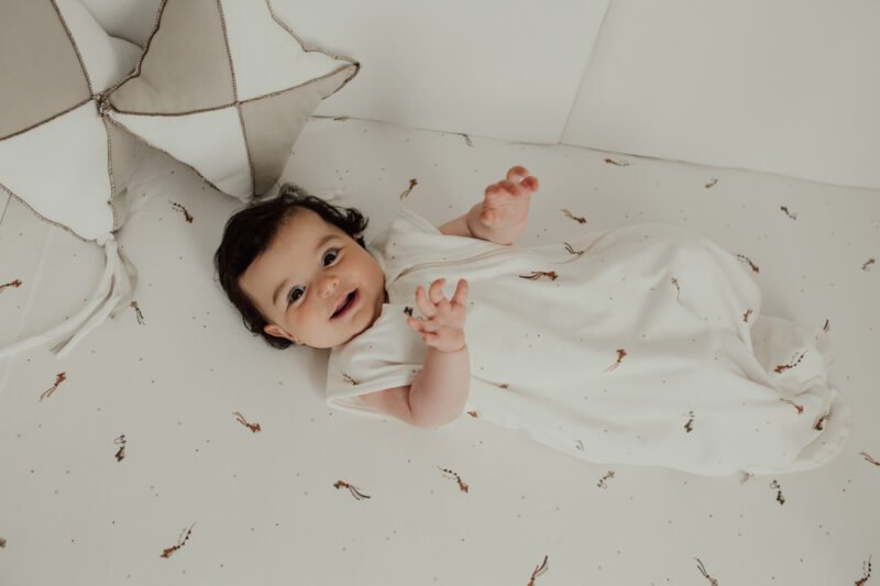 Bebé acostado sonriendo con saco pijama de verano 0-6 meses con estampado de cometas en algodón orgánico de Sonpetit Barcelona.